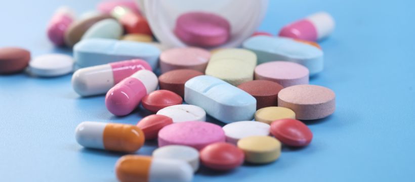 The benefits of magnesium for women. Image shows a blue background with multicoloured pills of different shapes and sizes in the foreground.